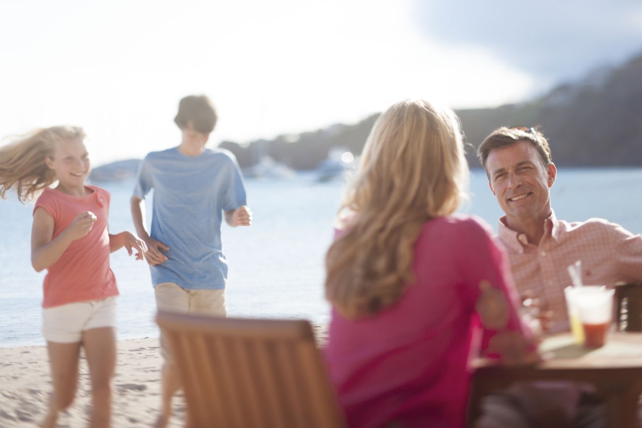 Couple dining on the beach with children running